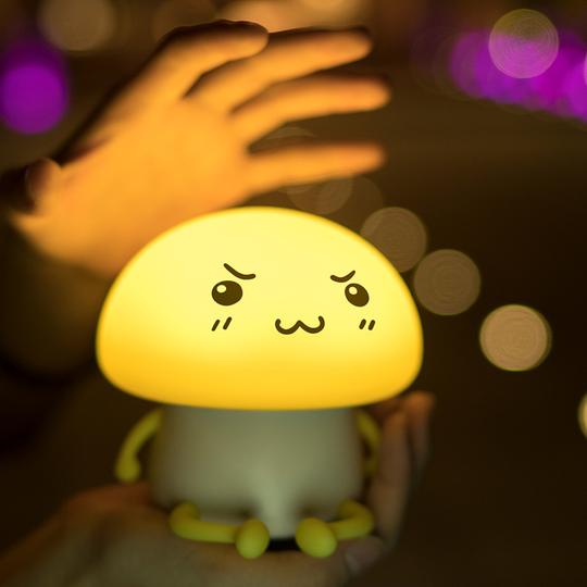 Children's night light with a face design held by a child, surrounded by blurred lights in the background.