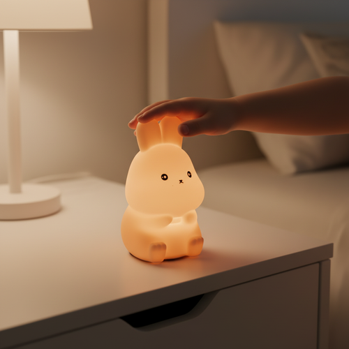 Cute rabbit-shaped night light being held by a hand on a bedside table.